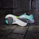 Et par Adidas Adizero Boston 13 herre løbesko i Flash Aqua/Cloud White/Lucid Lemon står på en våd, stenbelagt sti; den ene sko står oprejst, den anden viser sålen. I baggrunden ses en buet korridor.