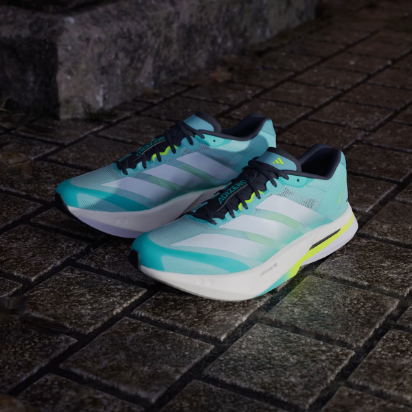 Et par Adidas Adizero Boston 13 herre løbesko i Flash Aqua/Cloud White/Lucid Lemon står side om side på en stenet udendørsflade nær et betontrin.