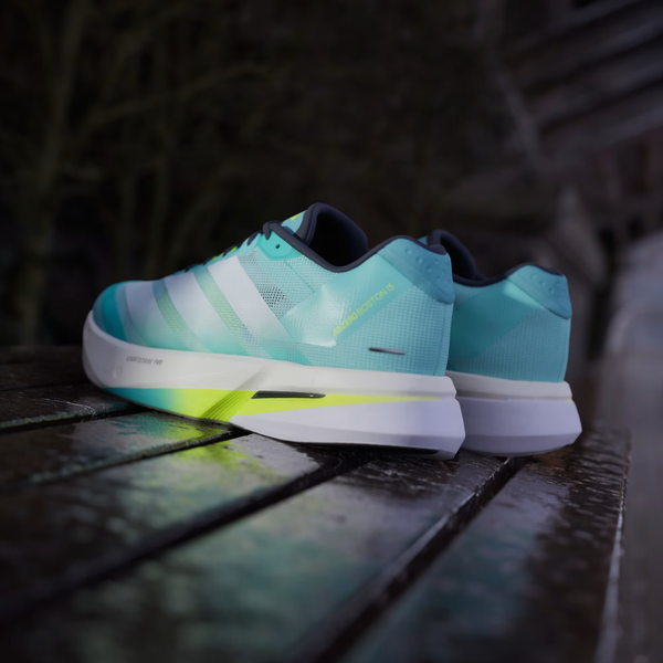 Et par Adidas Adizero Boston 13 herre løbesko i Flash Aqua/Cloud White/Lucid Lemon hviler på en våd træoverflade udendørs.