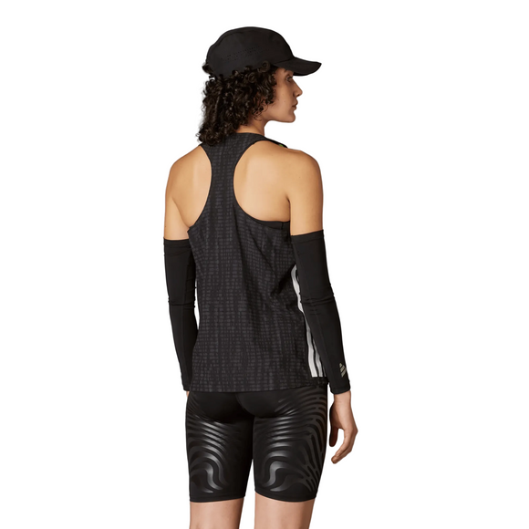 En person står med ryggen til i en sort Adidas Adizero Singlet, Dame, Carbon/Black, fremstillet af genbrugspolyester, med sorte ærmer og mønstrede sorte shorts på en almindelig grå baggrund.