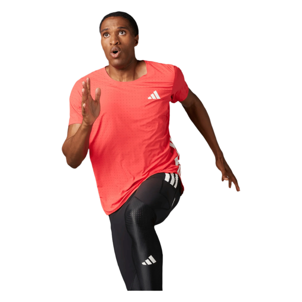 En mand i en Semi Lucid Red Adizero Running Tee og sorte Adidas-leggings løber fremad med et fokuseret blik og bøjet arm. Den åndbar løbe-T-shirt, lavet af genanvendt polyester, er fra Adidas. Baggrunden er almindelig hvid.