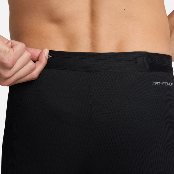 Et nærbillede viser en person, der trækker i linningen på sorte Nike AeroSwift ADV Running Tights, Herre, Black/Summit White, der fremhæver premium løbetights herre-stilen og Dri-FIT ADV-teksten på højre side.