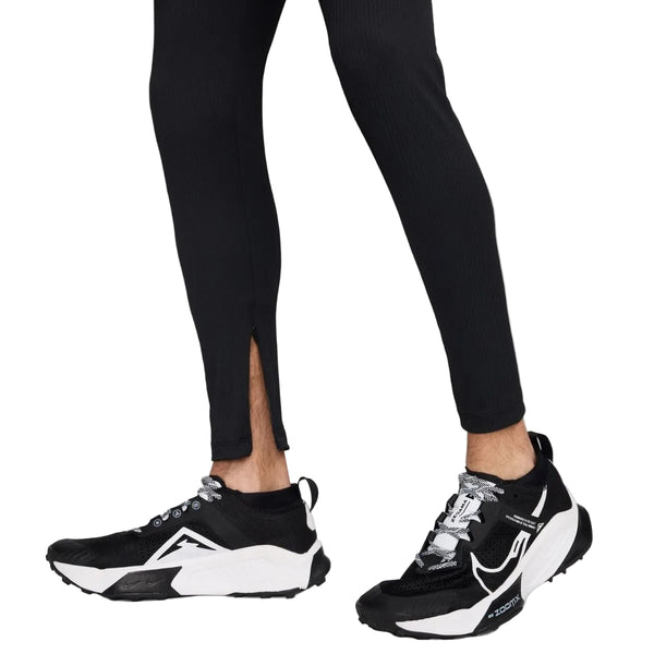 En person ses fra knæene og ned mod en hvid baggrund iført Nike AeroSwift ADV løbetights til mænd i Black/Summit White med en lille slids i siden nær anklen, sammen med sorte og hvide sneakers.