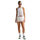 En kvinde bærer Nike AeroSwift Cropped Tank Top, Dame, Off White/Black med hvide sportsshorts, sokker, løbesko og solbriller, mens hun står på en hvid baggrund.