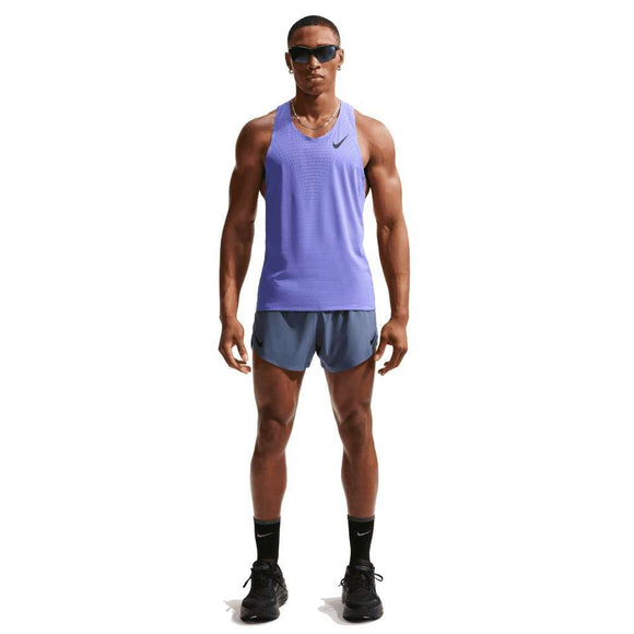 En mand står med front mod solbriller, sorte sokker og sko, blå shorts og en Nike AeroSwift Running Singlet, Herre, Sapphire/Black - ideel til løbetræning - mod en almindelig hvid baggrund.