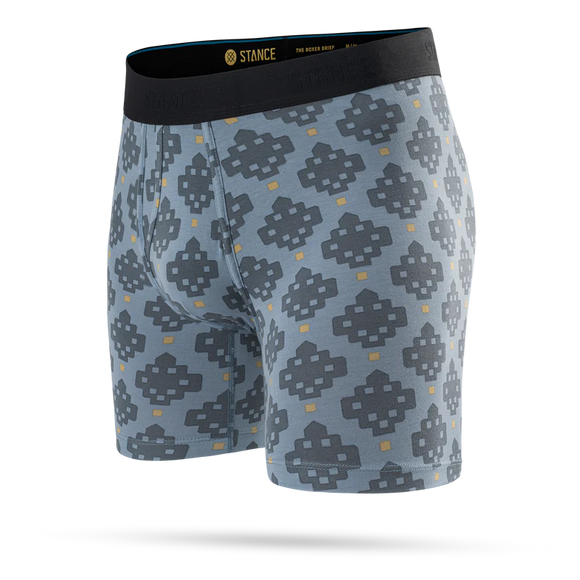 Stance Alhambra Wholester, Herre, Blå er et par lyseblå boxershorts til mænd med et gentagende geometrisk mønster i mørkegrå og gul. De er fremstillet af det luksuriøse Butter Blend-materiale, der sikrer optimal komfort, og er afsluttet med en sort linning med mærkelogo. Produktet vises på en ensfarvet hvid baggrund.