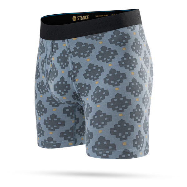Stance Alhambra Wholester, Herre, Blå er et par lyseblå boxershorts til mænd med et gentagende geometrisk mønster i mørkegrå og gul. De er fremstillet af det luksuriøse Butter Blend-materiale, der sikrer optimal komfort, og er afsluttet med en sort linning med mærkelogo. Produktet vises på en ensfarvet hvid baggrund.