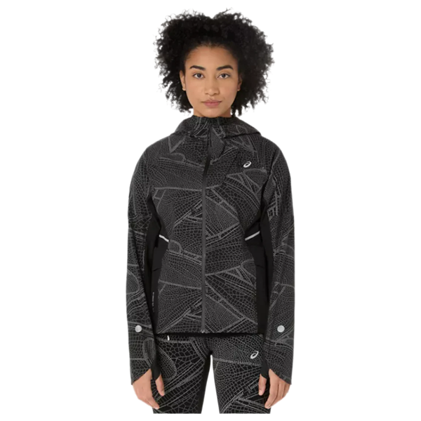 En person med krøllet hår viser Asics Limited Series Lite-Show Jacket, Dame, i Performance Black og geometrisk mønstrede bukser frem mod en hvid baggrund. Jakkens høje krave skiller sig ud.