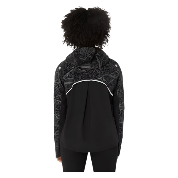 En kvinde med krøllet hår, set bagfra, er iført Asics Limited Series Lite-Show Jacket i Performance Black. Den har et hvidt geometrisk mønster, en reflekterende vandret stribe bagpå, lange ærmer og en afslappet pasform.