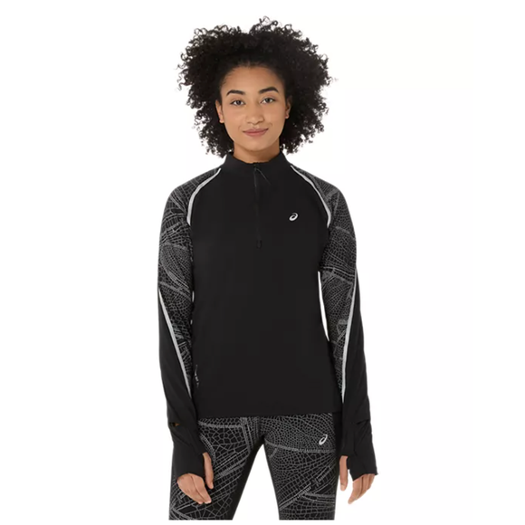 En kvinde med krøllet hår bærer den sorte Asics Limited Series Lite-Show Ls Top til kvinder med reflekterende detaljer og mønstrede ærmer sammen med matchende leggings, der står på en almindelig hvid baggrund.