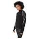En person med krøllet hår bærer Asics Limited Series Lite-Show Ls Top, Dame, i Performance Black med matchende mønstrede leggings og refleksdetaljer, mens hun står lidt sidelæns mod en hvid baggrund.