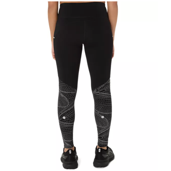 En kvinde ses bagfra iført Asics Limited Series Lite-Show Tight, Dame i Performance Black med hvide geometriske mønstre, parret med sorte sneakers og en sort top, stående mod en almindelig hvid baggrund.