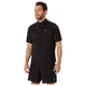 En mand med kort mørkt hår og skæg er iført Asics Metarun Packable Gilet, Herre, Performance Black over en sort skjorte og shorts - alle med Asics-logo. Han kigger lidt til venstre og smiler.