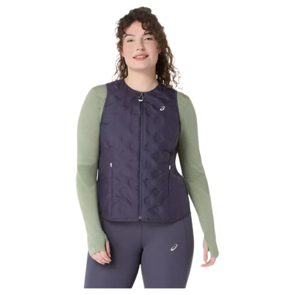 En person ser frem for sig i en Asics Nagino Run Padded Gilet, Dame, Indigo Fog, med lynlås over en lysegrøn langærmet top og mørke leggings. Et lille logo på brystet er synligt. Baggrunden er almindelig hvid.