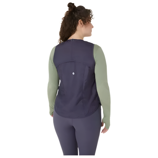 En person med krøllet hår står med ryggen til kameraet mod en hvid baggrund iført en Asics Nagino Run Padded Gilet til kvinder i Indigo Fog over en grøn langærmet top og matchende leggings.
