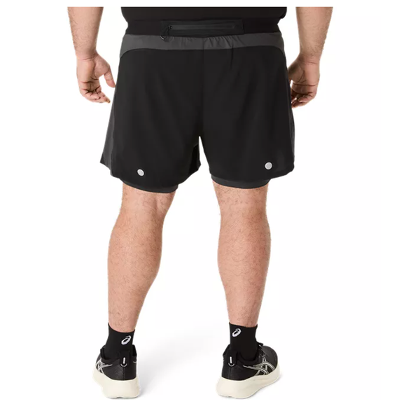 En person står med ryggen til kameraet iført Asics Road 2-N-1 5In Shorts i Performance Black/Graphite Grey, sorte ankelsokker og hvide sportssko på en almindelig hvid baggrund.