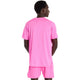 En person med kort hår står og kigger væk fra kameraet iført en New Balance Athletics T-Shirt, Herre, Pink Heat Heather og matchende lyserøde shorts på en almindelig hvid baggrund.