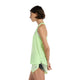 En person står i profil iført en New Balance Athletics Tank, Dame, Afterglow Heather/Slate Grey med matchende prikkede shorts og hænderne foldet bag ryggen mod en almindelig hvid baggrund. Toppen er fremstillet af åndbart materiale.
