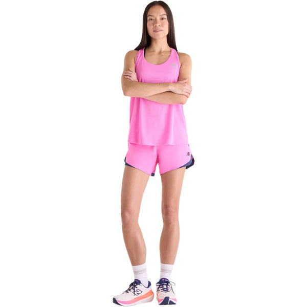 En kvinde står med armene over kors iført en New Balance Athletics Tank for dame i Pink Heat Heather/Slate Grey, matchende træningstøj, hvide strømper og pink-hvide løbesko. Hun ser fremad mod en hvid baggrund.