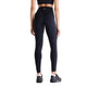 En person iført en sort sports-BH, sorte New Balance Athletics Heat High Rise Legging 27″ med NB HEAT-teknologi og sorte sneakers står med ryggen til kameraet foran en hvid baggrund. Disse avancerede Athletics Heat High Rise Legging 27″ til kvinder fra New Balance er designet med henblik på både komfort og ydeevne.
