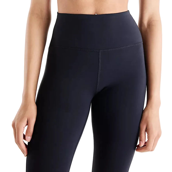 Der ses en person fra taljen til midt på låret iført et par New Balance Athletics Heat High Rise Legging 27″ i sort, kombineret med en crop top. Personens arme hænger afslappet ned langs siden på en ensfarvet hvid baggrund.