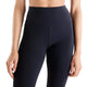 Der ses en person fra taljen til midt på låret iført et par New Balance Athletics Heat High Rise Legging 27″ i sort, kombineret med en crop top. Personens arme hænger afslappet ned langs siden på en ensfarvet hvid baggrund.