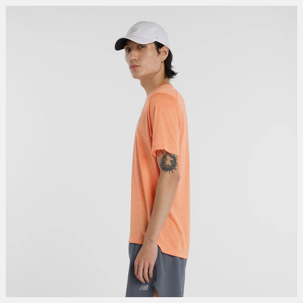 En person med mørkt hår og en tatovering på venstre overarm står i profil iført en lysegrå kasket, grå shorts og New Balance Athletics T-Shirt, Herre, Aae med hurtigtørrende teknologi på en hvid baggrund.