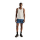En mand står med ansigtet vendt fremad iført en grå løbetank til mænd, nærmere bestemt New Balance Athletics Tank i farven Athletic Grey, samt blå mønstrede shorts, sorte sokker og sorte løbesko, foran en ensfarvet hvid baggrund.