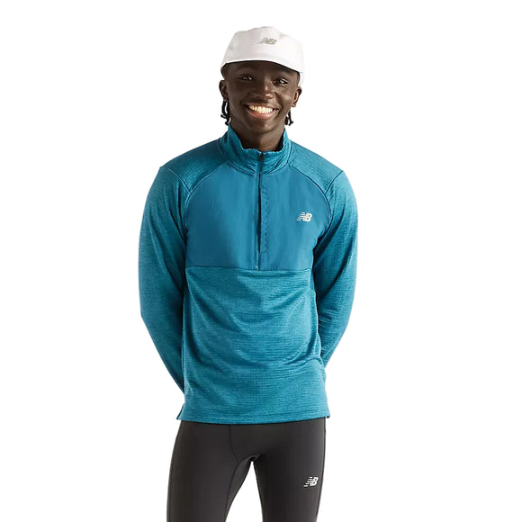 En mand iført en blågrøn New Balance Athletics Heat Grid 1/2 Zip, Herre, Streamsong-trøje med høj krave og sorte leggings.