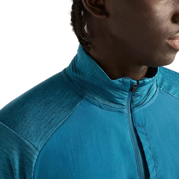 Et nærbillede af en blågrøn New Balance Athletics Heat Grid 1/2 Zip, Herre, Streamsong-løbetrøje med høj krave og en lodret lynlås på brystet.