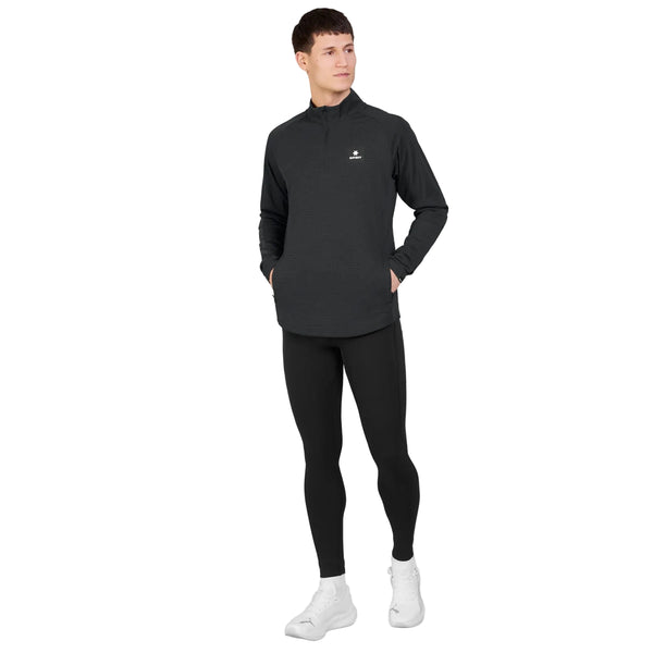 En person står med hænderne i lommerne iført en sort Saysky Blaze Half Zip Lightweight Fleece til mænd, kombineret med sorte leggings og hvide sneakers, og vender let mod venstre foran en ensfarvet hvid baggrund.