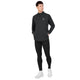 En person står med hænderne i lommerne iført en sort Saysky Blaze Half Zip Lightweight Fleece til mænd, kombineret med sorte leggings og hvide sneakers, og vender let mod venstre foran en ensfarvet hvid baggrund.