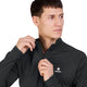 Der vises en person, der trækker lynlåsen op i kraven på Saysky Blaze Half Zip Light-weight Fleece (Herre, Sort), en mørk, langærmet sportstrøje med en lille hvid stjerne og SAYSKY-logoet. Den lette fleece-trøje giver ekstra komfort, mens personen kigger let til siden med et neutralt udtryk foran en ensfarvet baggrund.