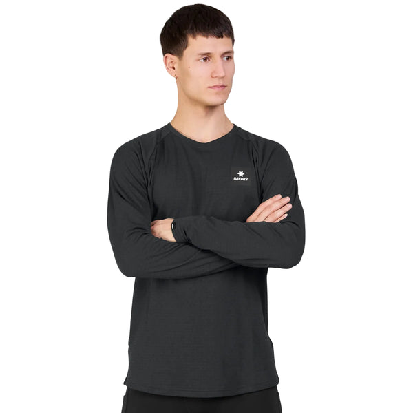 En person iført en svedabsorberende, letvægts-trøje – nemlig Saysky Blaze Long Sleeve Light-Weight Fleece til herre i sort med et lille hvidt logo på brystet – står med armene over kors og kigger mod venstre. Baggrunden er ensfarvet og lys.
