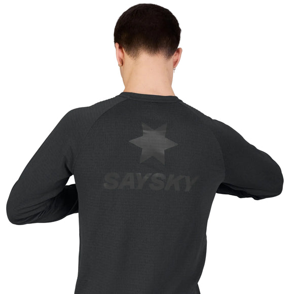 En person står med ryggen til kameraet og har en sort Saysky Blaze langærmet letvægtsfleece til mænd på, hvor der på ryggen er trykt et stjernesymbol og ordet »SAYSKY«. Den ensfarvede, lyse baggrund fremhæver den svedabsorberende komfort ved denne højtydende trøje.