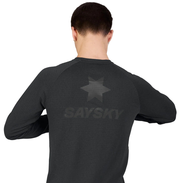 En person står med ryggen til kameraet og har en sort Saysky Blaze langærmet letvægtsfleece til mænd på, hvor der på ryggen er trykt et stjernesymbol og ordet »SAYSKY«. Den ensfarvede, lyse baggrund fremhæver den svedabsorberende komfort ved denne højtydende trøje.