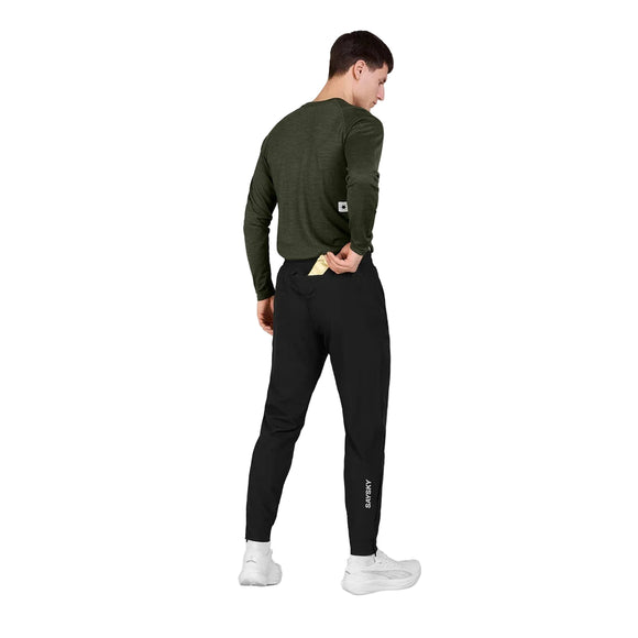 En person står med ryggen til og har en grøn langærmet skjorte og sorte unisex-bukser af mærket Blaze fra Saysky på, kombineret med hvide sneakers. Personen løfter let skjortens bagkant med den ene hånd. Baggrunden er helt hvid.