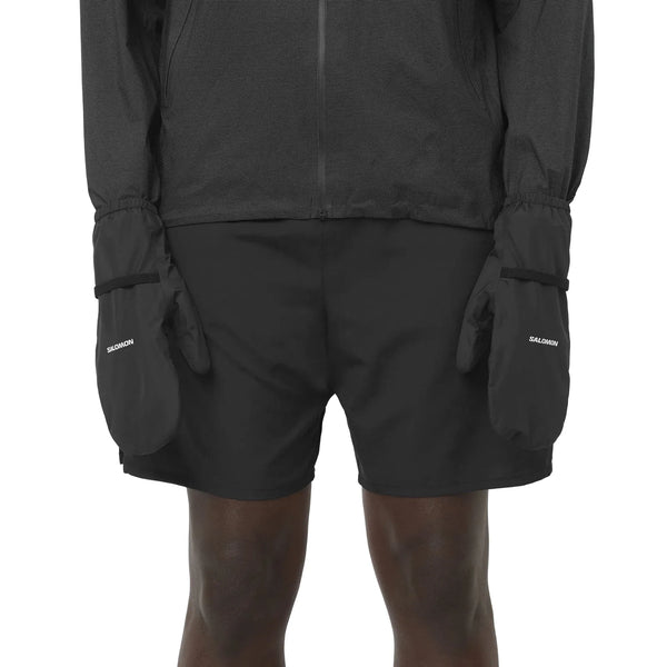 En person iført sorte løbeshorts og en langærmet jakke med Salomon Bonatti Pro WP Mitten, Unisex, Deep Black trukket ned over hænderne.