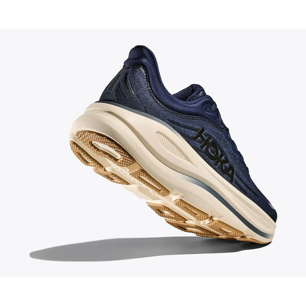 A Hoka Bondi 9 herre løbesko i Midnight Blue/Varsity Navy vises fra en vinkel, der fremhæver den tykke, beige sål for maksimal komfort og greb. HOKA-logoet er tydeligt på siden.