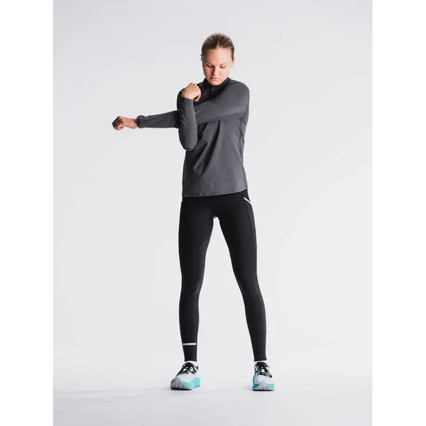 Iført Fusion's Long Tight i SuperBlack står en person på en ensfarvet baggrund og strækker sin venstre arm over brystet med hovedet let nedad.