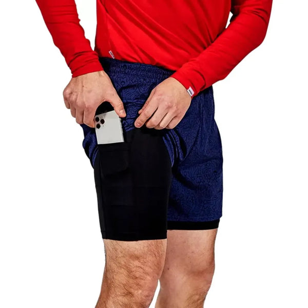 En person iført en rød langærmet skjorte og Saysky CC Pace 2 in 1 Shorts 5" (Herre, Blue) lægger en smartphone i den sorte sidelomme. Kun overkroppen og overbenene er synlige.