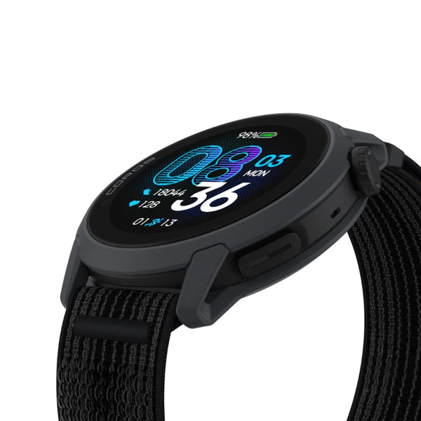 Et nærbillede af COROS Pace 4 Multisport Watch in Nylon Black viser den runde urskive med tid, dato, puls, skridt og batteri på en farverig skærm. Uret har en sort vævet rem og indbygget GPS, set fra et vinklet sideperspektiv.