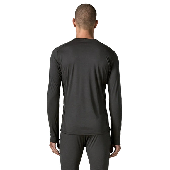 En person står med ryggen til kameraet og er iført en langærmet trøje og et par bukser i samme farve. Trøjen er en Patagonia Cap LW Crew til mænd i sort, et ultralet baselayer. Baggrunden er ensfarvet hvid.