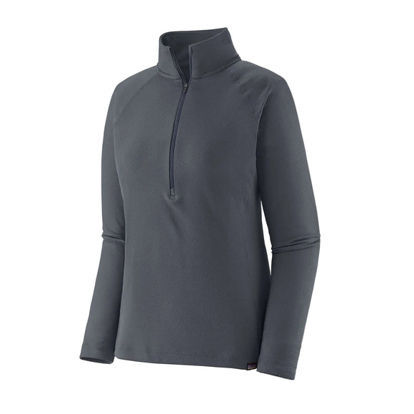 Patagonia Cap Midweight Zip Neck til kvinder i Smolder Blue er en langærmet pullover med mock neck og halv lynlås foran, der har et subtilt struktureret mønster inspireret af klassiske baselayers. Vises på en hvid baggrund.