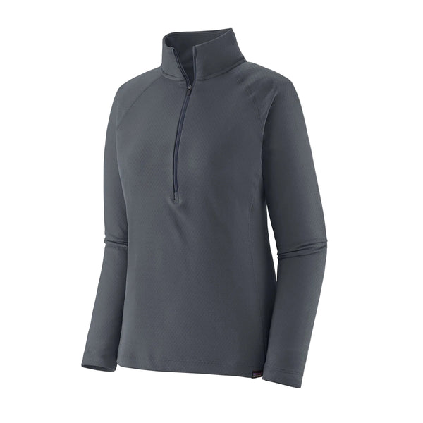 Patagonia Cap Midweight Zip Neck til kvinder i Smolder Blue er en langærmet pullover med mock neck og halv lynlås foran, der har et subtilt struktureret mønster inspireret af klassiske baselayers. Vises på en hvid baggrund.