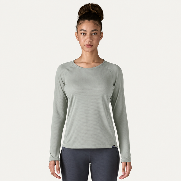 En kvinde med håret sat op i en knold har en Patagonia Cap Midweight Crew-undertøjsbluse i farven »Sleet Green« og mørke leggings på. Hun står med ansigtet vendt fremad foran en ensfarvet hvid baggrund.