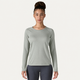 En kvinde med håret sat op i en knold har en Patagonia Cap Midweight Crew-undertøjsbluse i farven »Sleet Green« og mørke leggings på. Hun står med ansigtet vendt fremad foran en ensfarvet hvid baggrund.