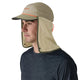 En person med en Patagonia Caped Merganzer Hat, unisex, River Rock Green, lavet af hurtigtørrende polyester med en påsat nakkeklap, og iført en mørkeblå skjorte, ser til venstre mod en almindelig hvid baggrund.