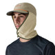 En mand bærer unisex Patagonia Caped Merganzer Hat i River Rock Green med en beige kasket, grøn kant og et påsat ventileret ansigts- og halsdæksel. Han står i en mørkeblå skjorte og kigger lidt til venstre mod en hvid baggrund.
