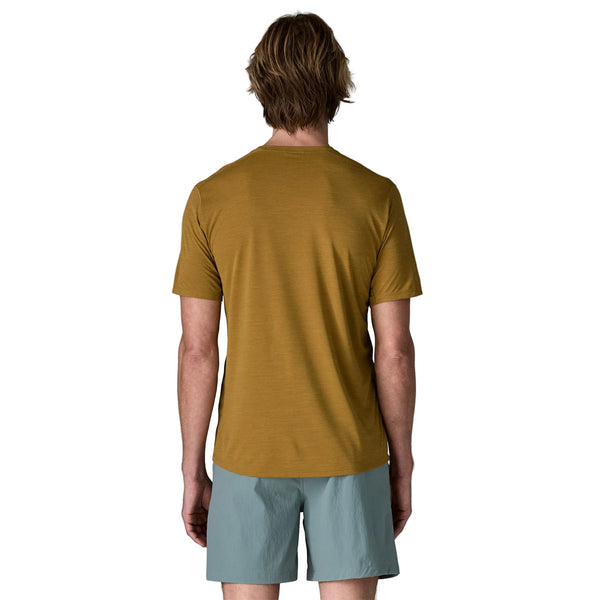 En person med lysebrunt hår ses bagfra iført en Patagonia Capilene Cool Ultra Shirt, Herre, i Bobcat Brown - Light Bobcat Brown X-Dye og lyseblå shorts på en almindelig hvid baggrund.